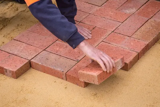 Clay pavers being set by hand into a sand bed