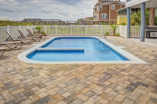 A paver pool deck screened by a row of arborvitae