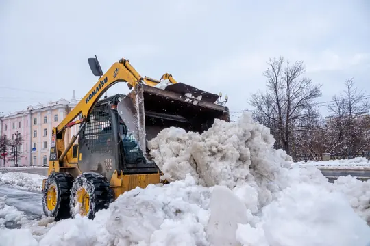 A compact loader clearing banked snow from a driveway