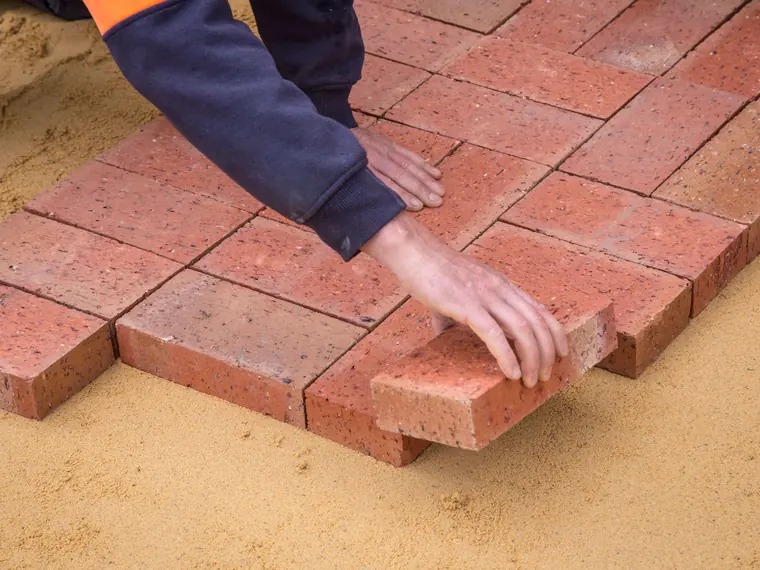Clay pavers being set by hand into a sand bed