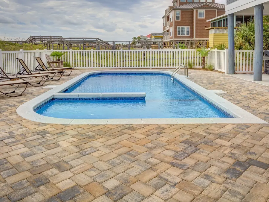 Cushioned outdoor furniture and a gas fire table on a paver deck beside a pool