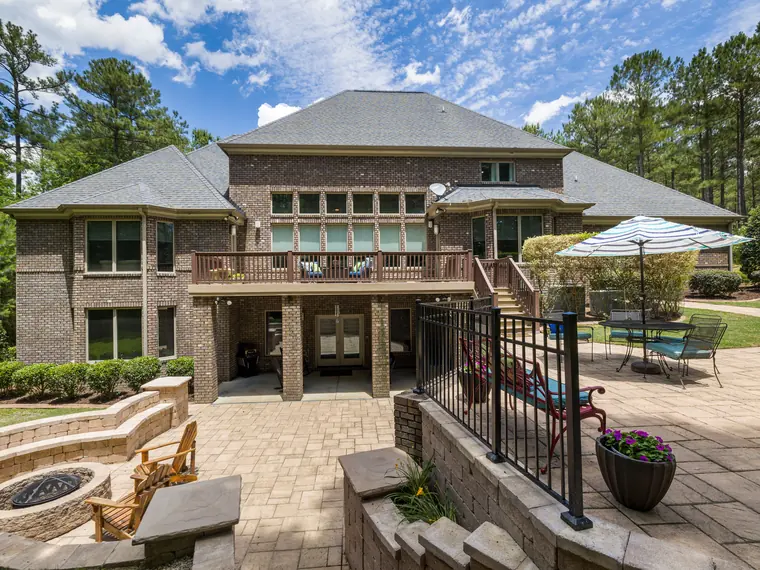 A pool surrounded by a wide paver deck and a white rail fence